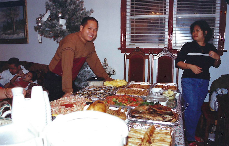 A photo of a man standing behind a table full of food.