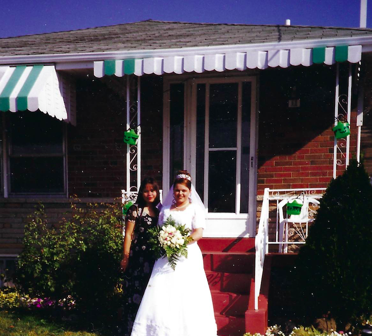 A bride taking a photo with a person in front of a house.