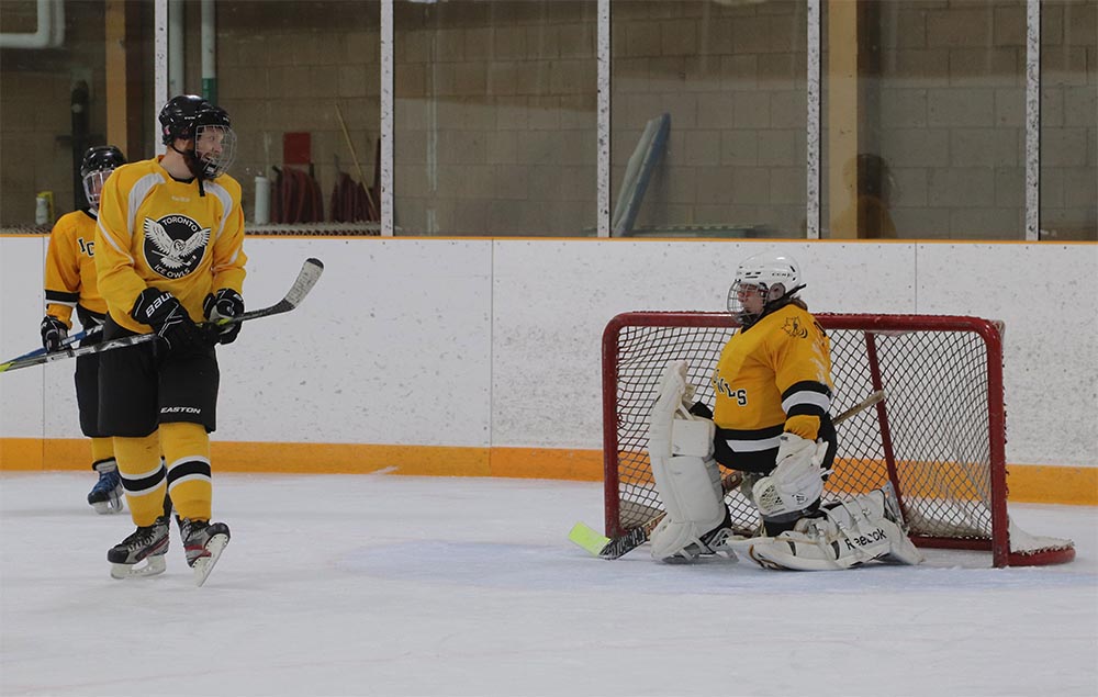Karen Rousseau is pictured in goalie gear, kneeling on one knee to chat to a teammate during a blind hockey game.
