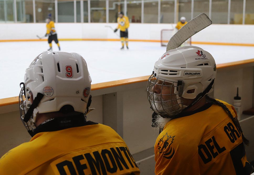 Mark DeMontis and Josep Del Grande chat on the bench during a Toronto Ice Owls blind hockey game.
