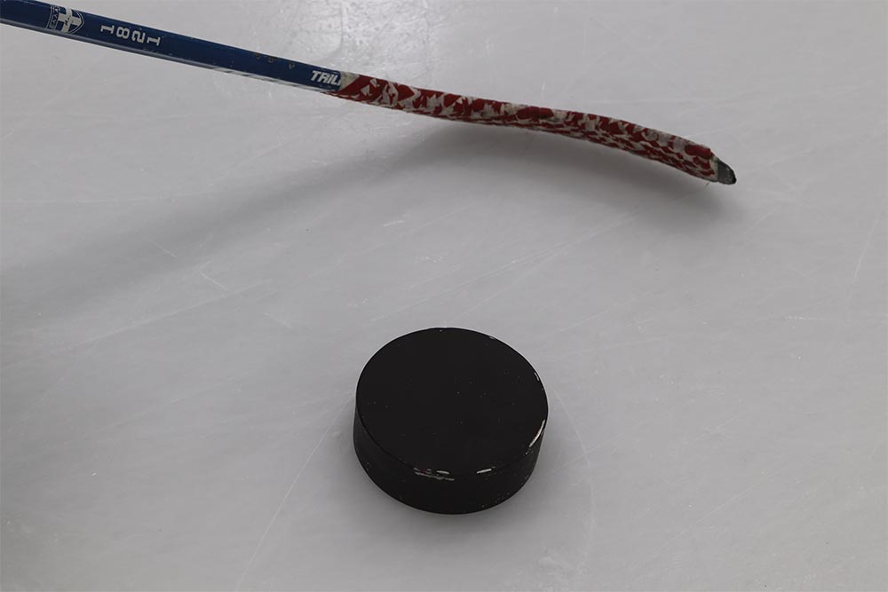 A blind hockey puck is pictured beside a hockey stick on ice.