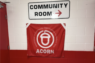 A white metal signed reading "Community Room" with an arrow pointing right. Underneath it, a fabric flag reading "ACORN Association of Community Organizations for Reform Now"