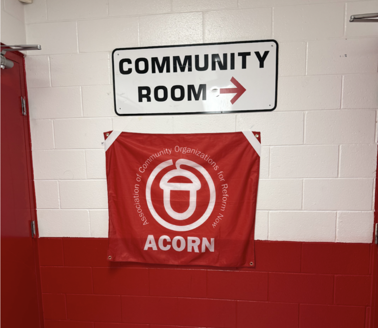 A white metal signed reading "Community Room" with an arrow pointing right. Underneath it, a fabric flag reading "ACORN Association of Community Organizations for Reform Now"