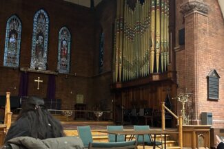 People seated in chairs inside a church, with a large pipe organ visible in the background