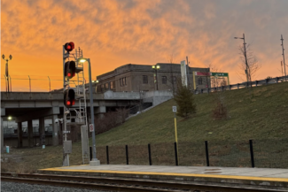 Railway crossing at sunset with orange sky and red signal lights and tracks.