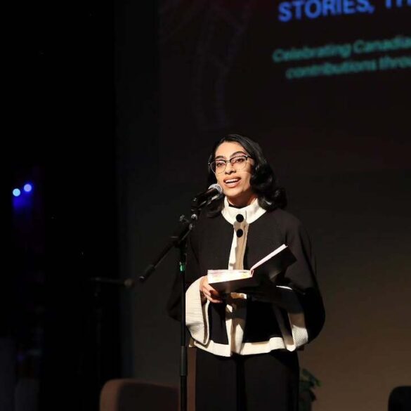 Person standing in front of a screen while talking into a microphone, with a book in their hand